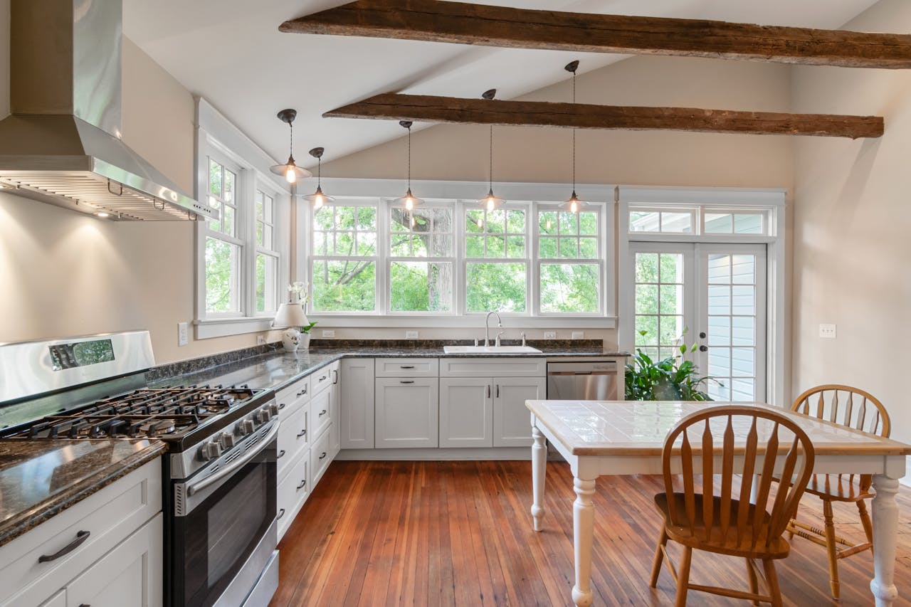 Bright kitchen interior featuring wooden beams, white cabinetry, and natural lighting.