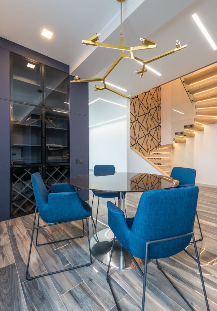 Home Stylish dining room featuring blue armchairs, glass table, and contemporary lighting. Ideal for modern homes.